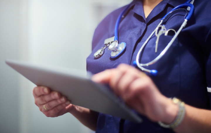 An NHS worker in a dark blue tunic using an electronic tablet