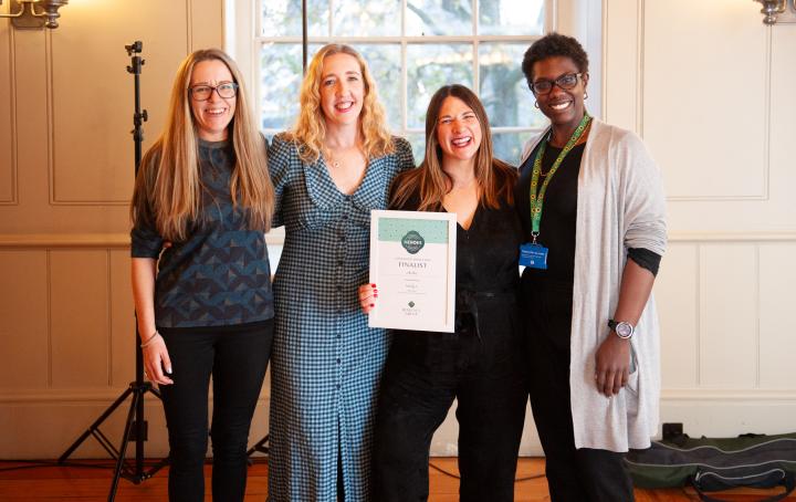 Four ladies stood together, smiling and looking at the camera as they are presented with a certificate