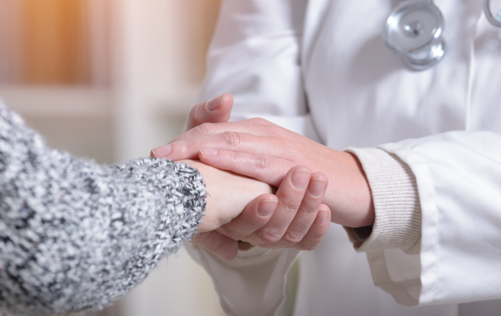 A healthcare professional holding the hand of their patient in compassion