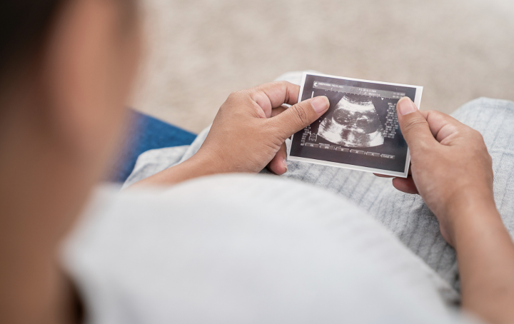 Person in hospital gown sits, holding baby scan. Sands logo is in top right corner.