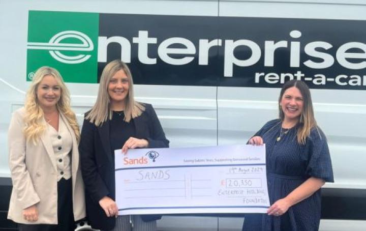 Three ladies stood infront of an Enterprise van holding a large cheque