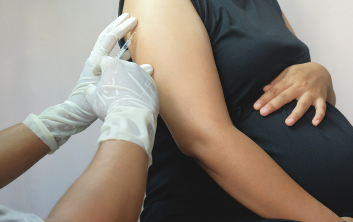 Pregnant woman receives Covid vaccination in her left arm by male nurse.