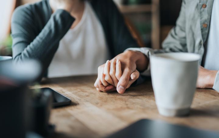 Image of couple holding hands on a table while drinking coffee