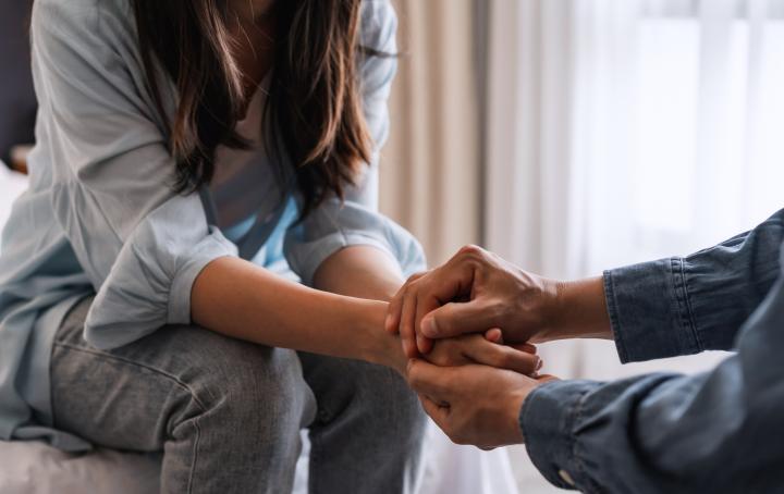 Two people sat down, no faces are in shot, but they are holding hands in a private moment