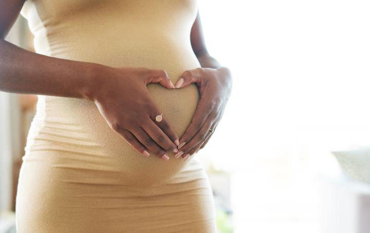A pregnant woman holding her hands in a heart shape on her pregnancy bump.