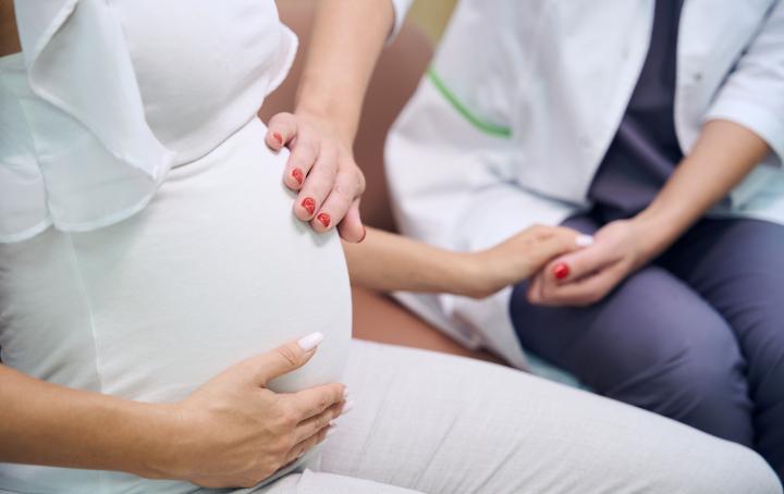 A pregnant person sits with one hand on her bump and the other holding a health professionals hand. The health professional has their spare hand on the pregnant person's bump