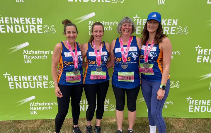 Four women wearing Sands running vests and their race medals, sml